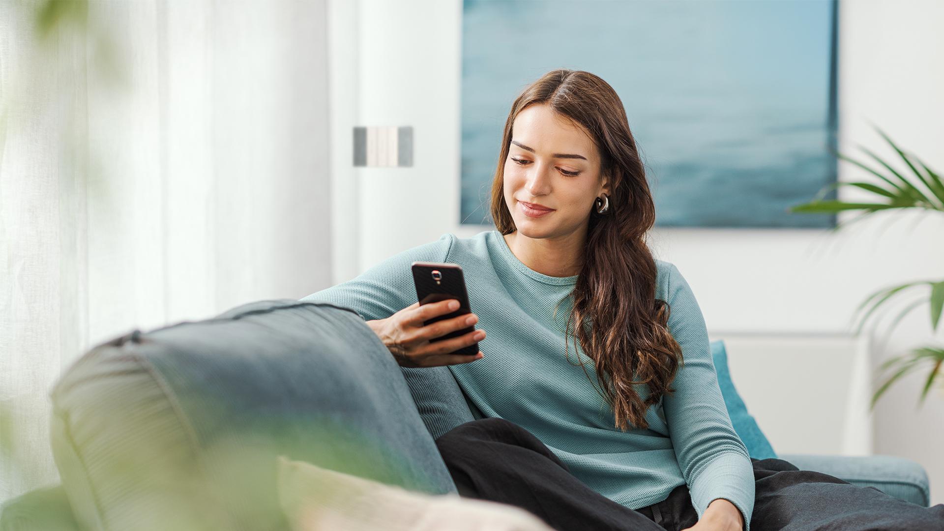 Una ragazza seduta sul divano guarda lo smartphone