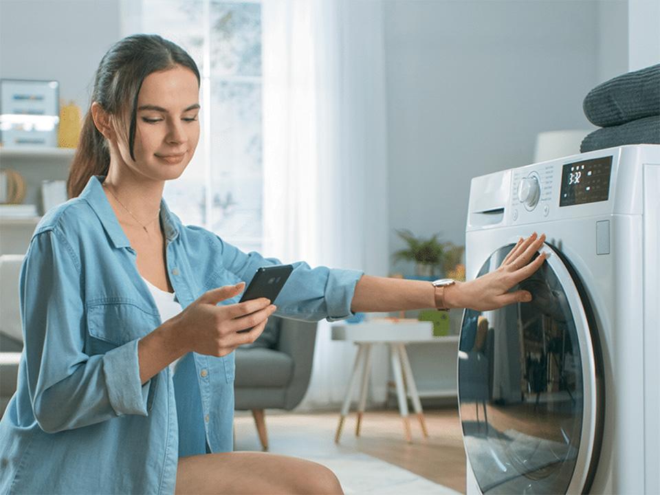 ragazza guarda lo smartphone e chiude la lavatrice