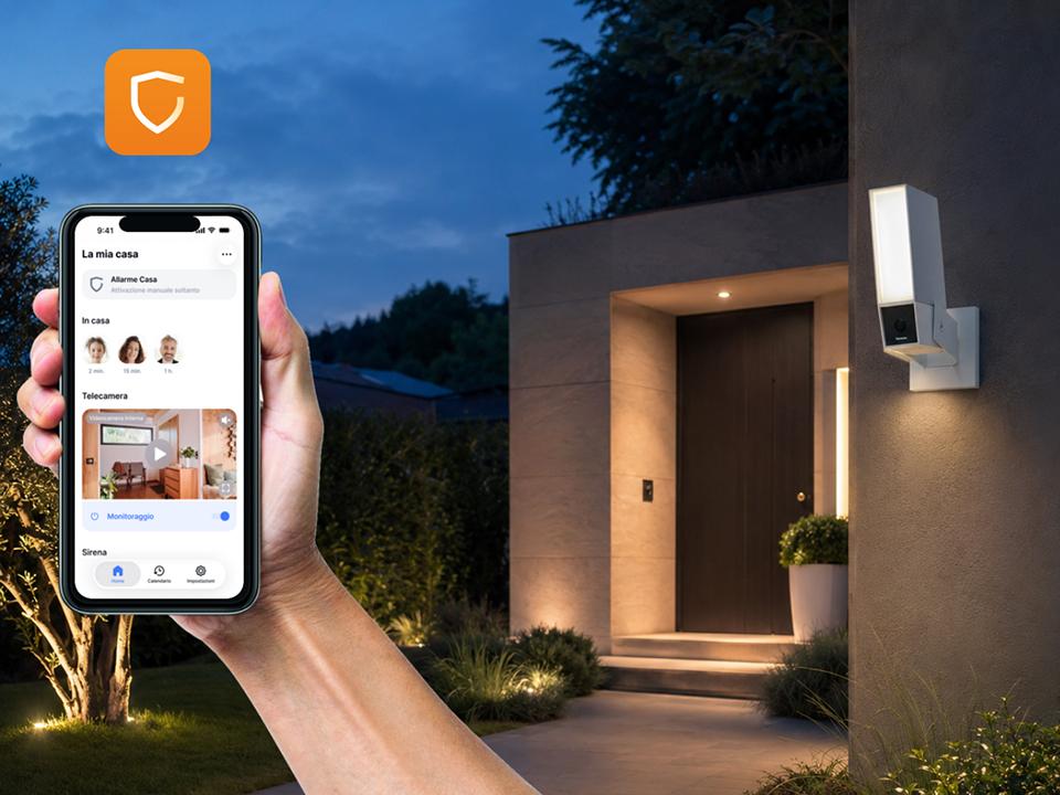 In primo piano, uno smartphone con Home+Security; sullo sfondo, una villa con telecamera Outdoor Original.