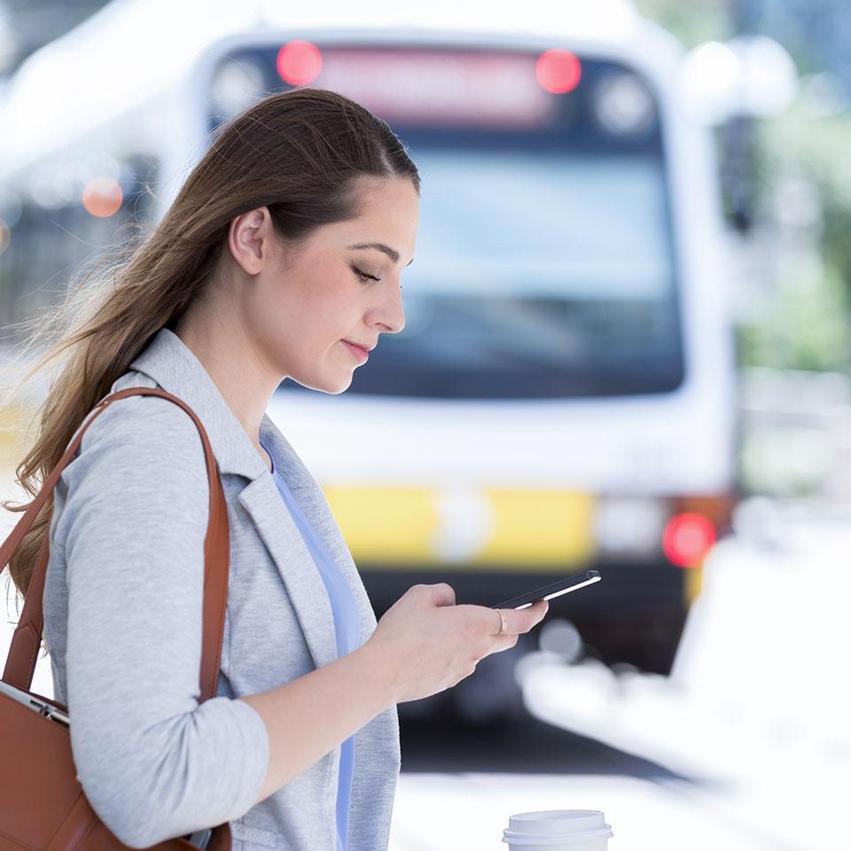 Una donna alla fermata del tram guarda lo smartphone